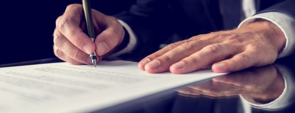 Signing legal document Retro image of lawyer signing important legal document on black desk. Over black background.