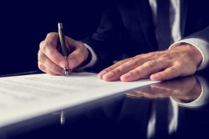 Retro image of lawyer signing important legal document on black desk. Over black background.